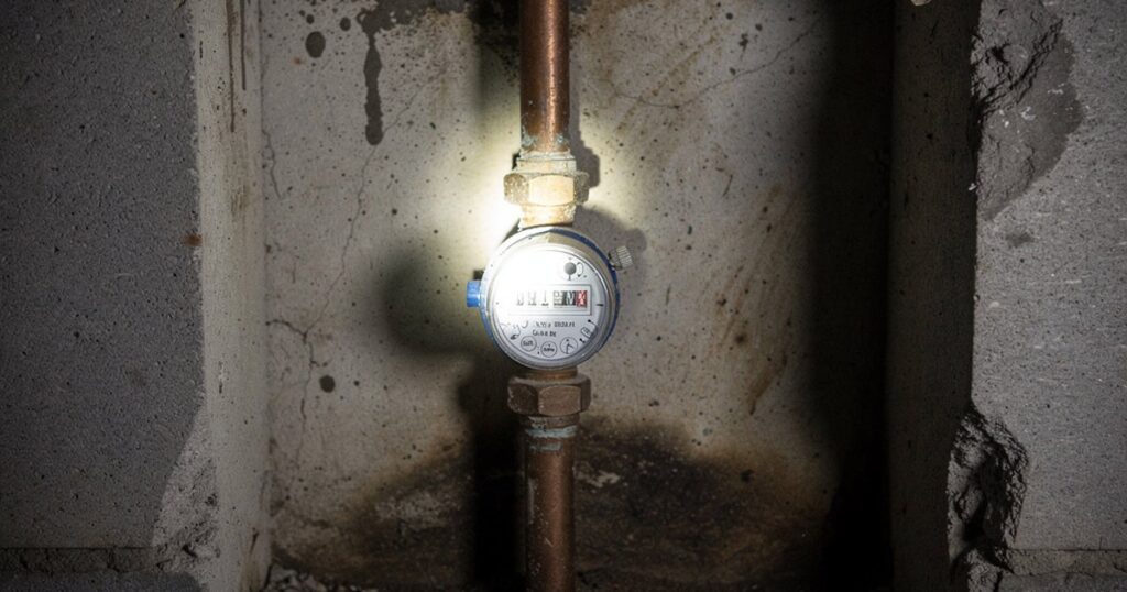 Un compteur d'eau dans une cave, éclairé à la lampe de poche, près d'un tuyau en cuivre